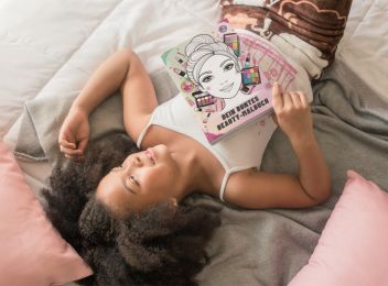 Grundschulmädchen liegt entspannt mit Beauty-Malbuch im Bett